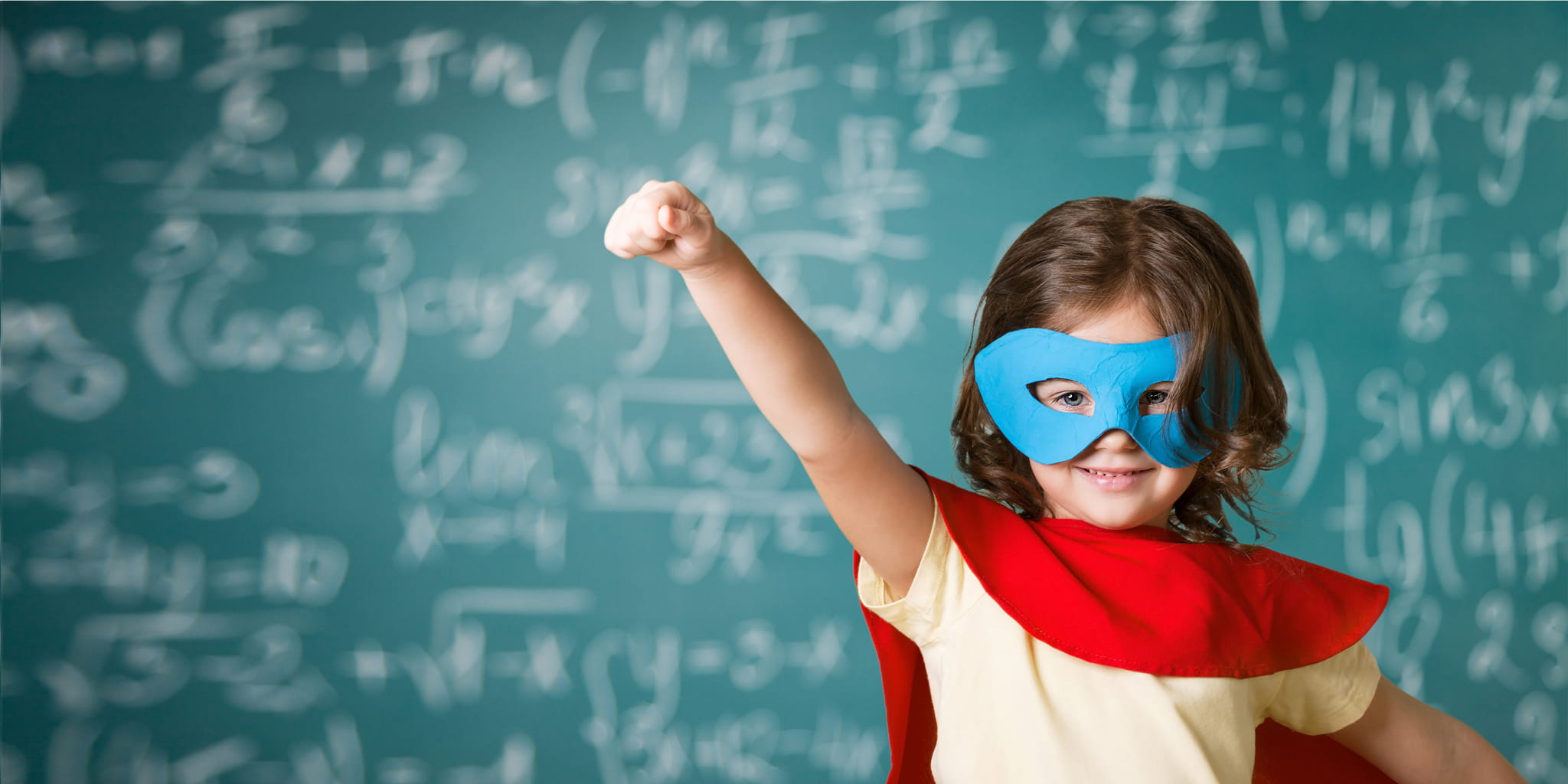 Kind in Superheldenkostüm steht vor einer Tafel