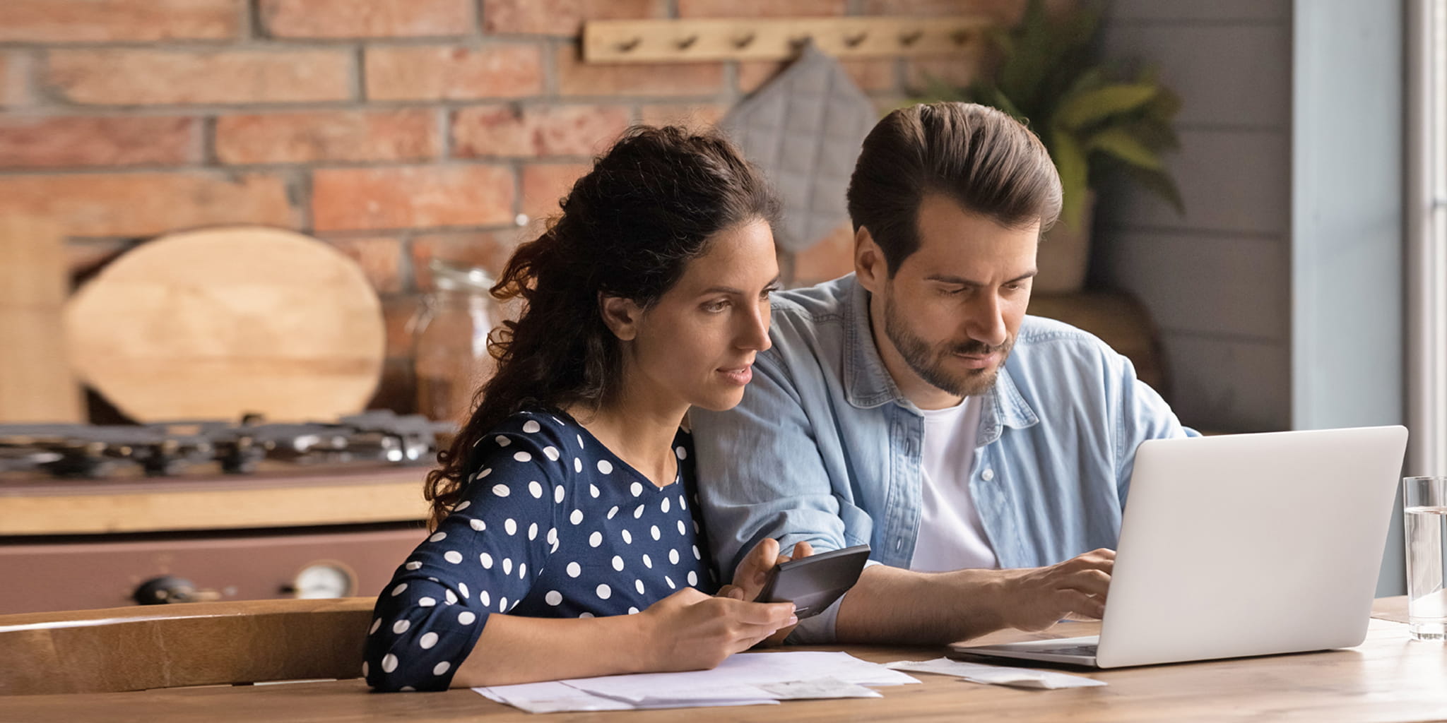 Zwei Erwachsene sitzen in der Küche an einem Laptop