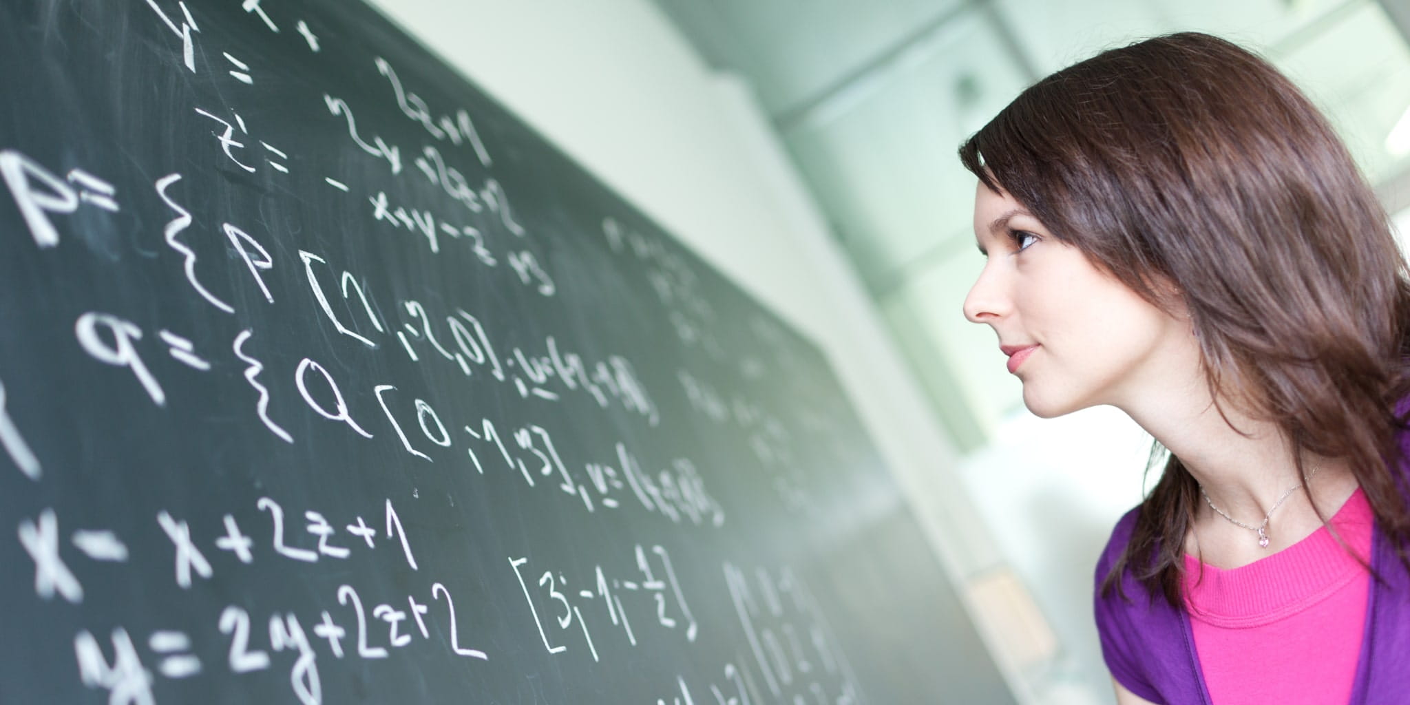 Frau steht vor einer Tafel und blickt auf mathematische Formeln