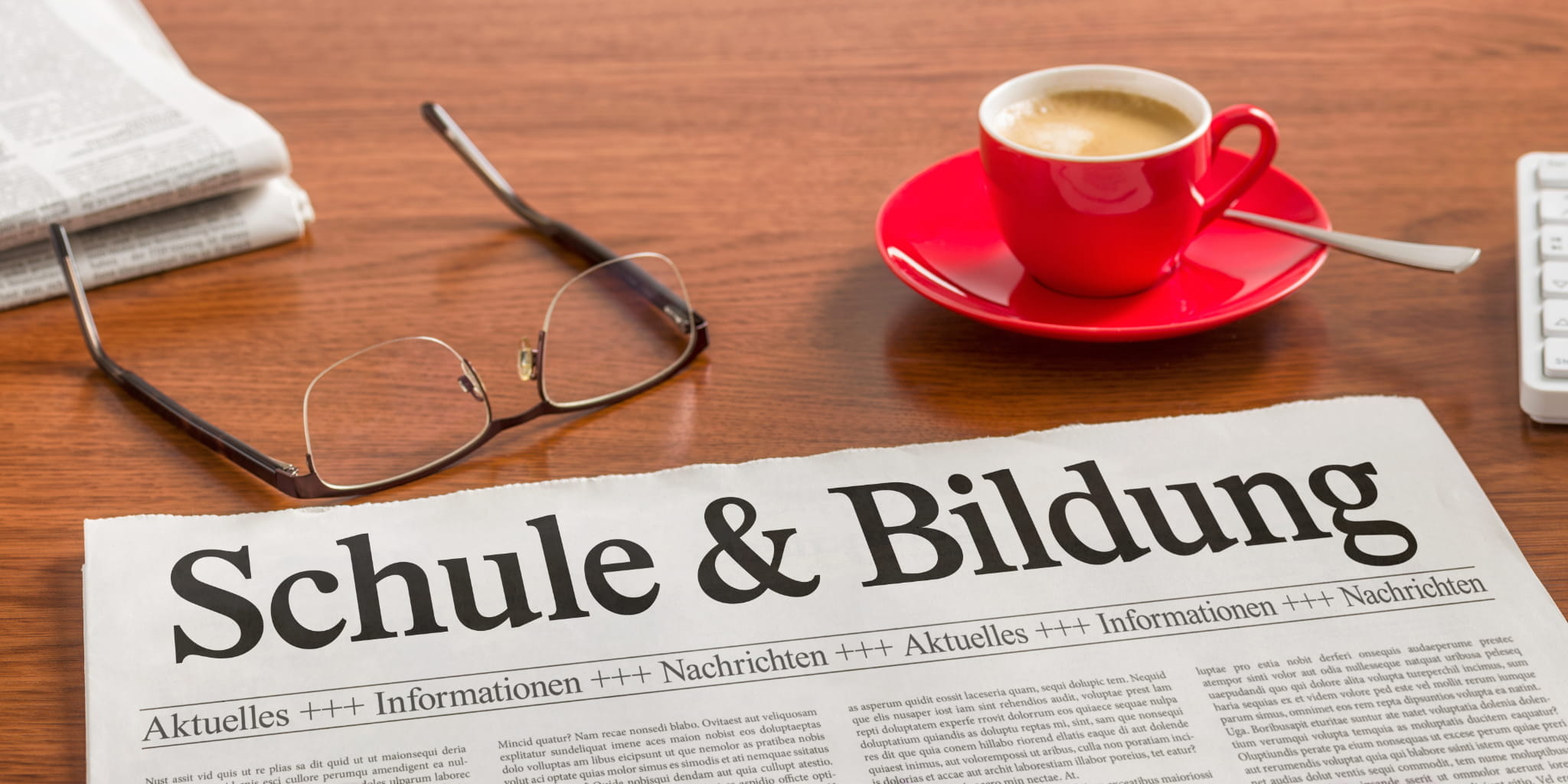 Schreibtisch mit einer Tasse Kaffee, einer Brille und einer Zeitung mit dem Titel Schule & Bildung