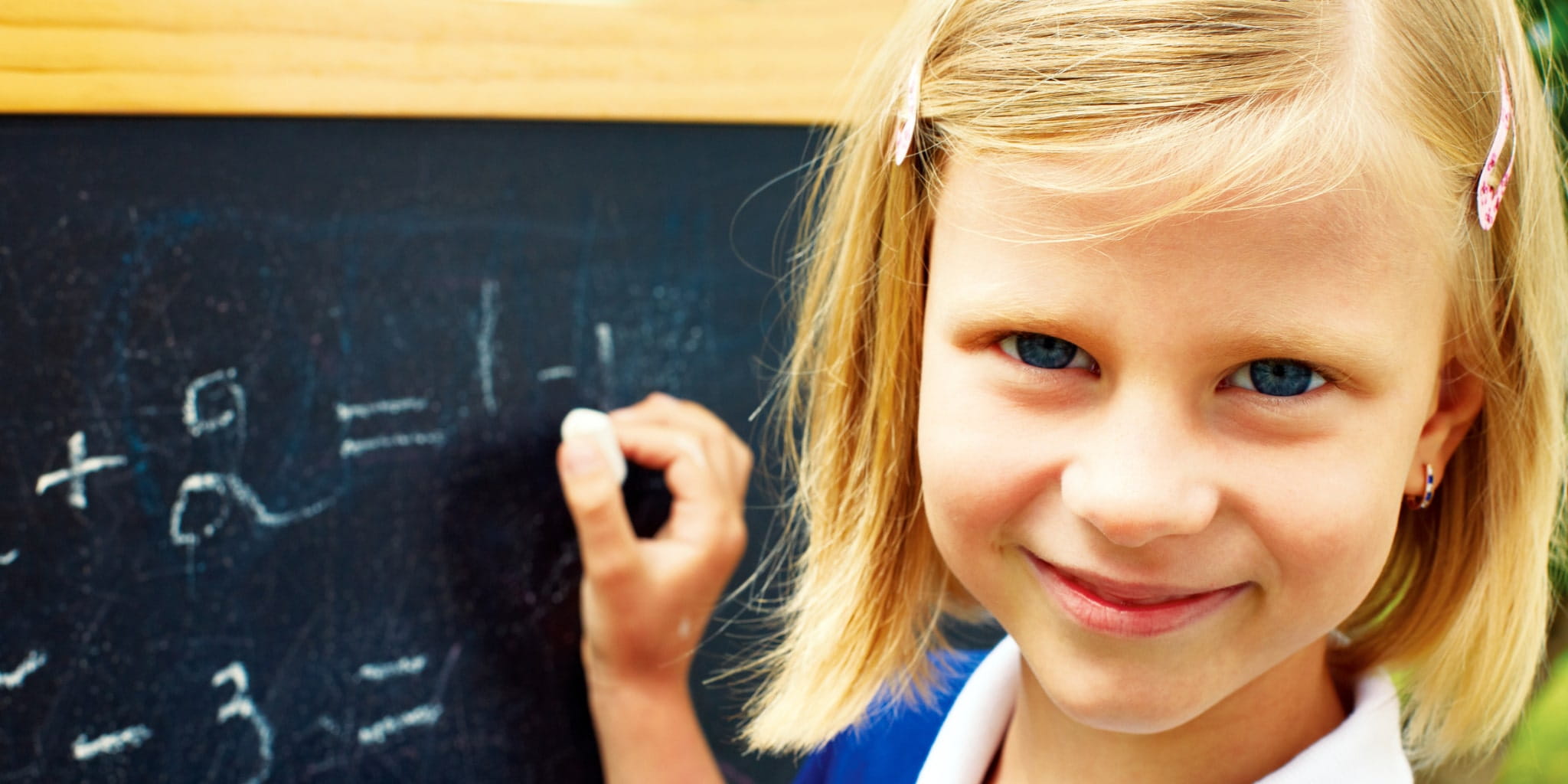 Ein Mädchen schreibt an einer Tafel und schaut zur Kamera