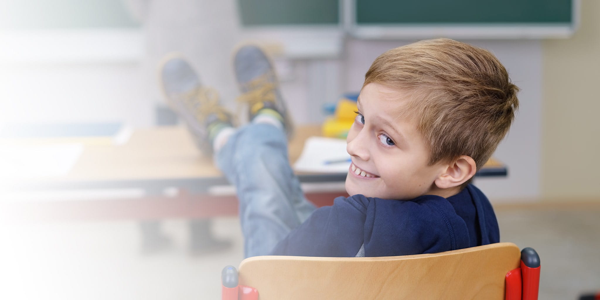 Kind sitz in der Schule und blickt lachend über seine Schuler