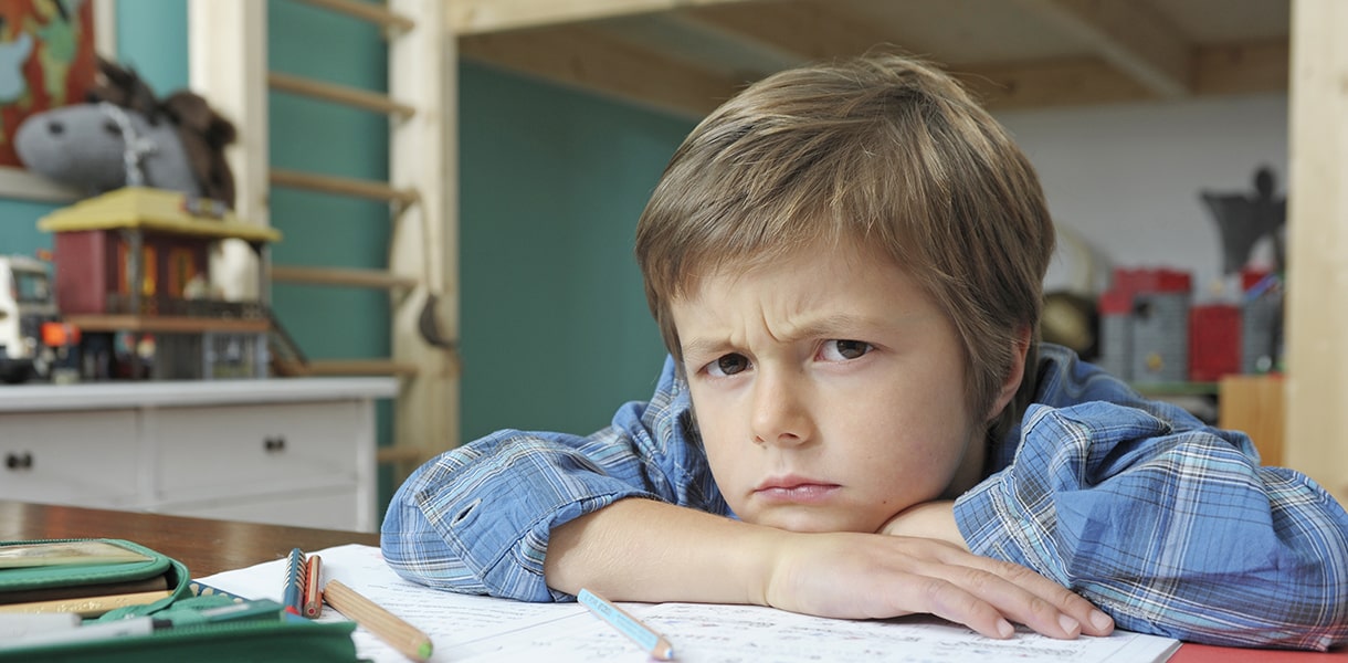 Ein Junge sitzt mit verkniffenem Gesicht in seinem Zimmer an Mathematik Hausaufgaben