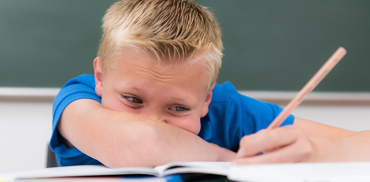 Ein Kind sitzt mit dem Kopf auf dem Arm an einem Schulheft